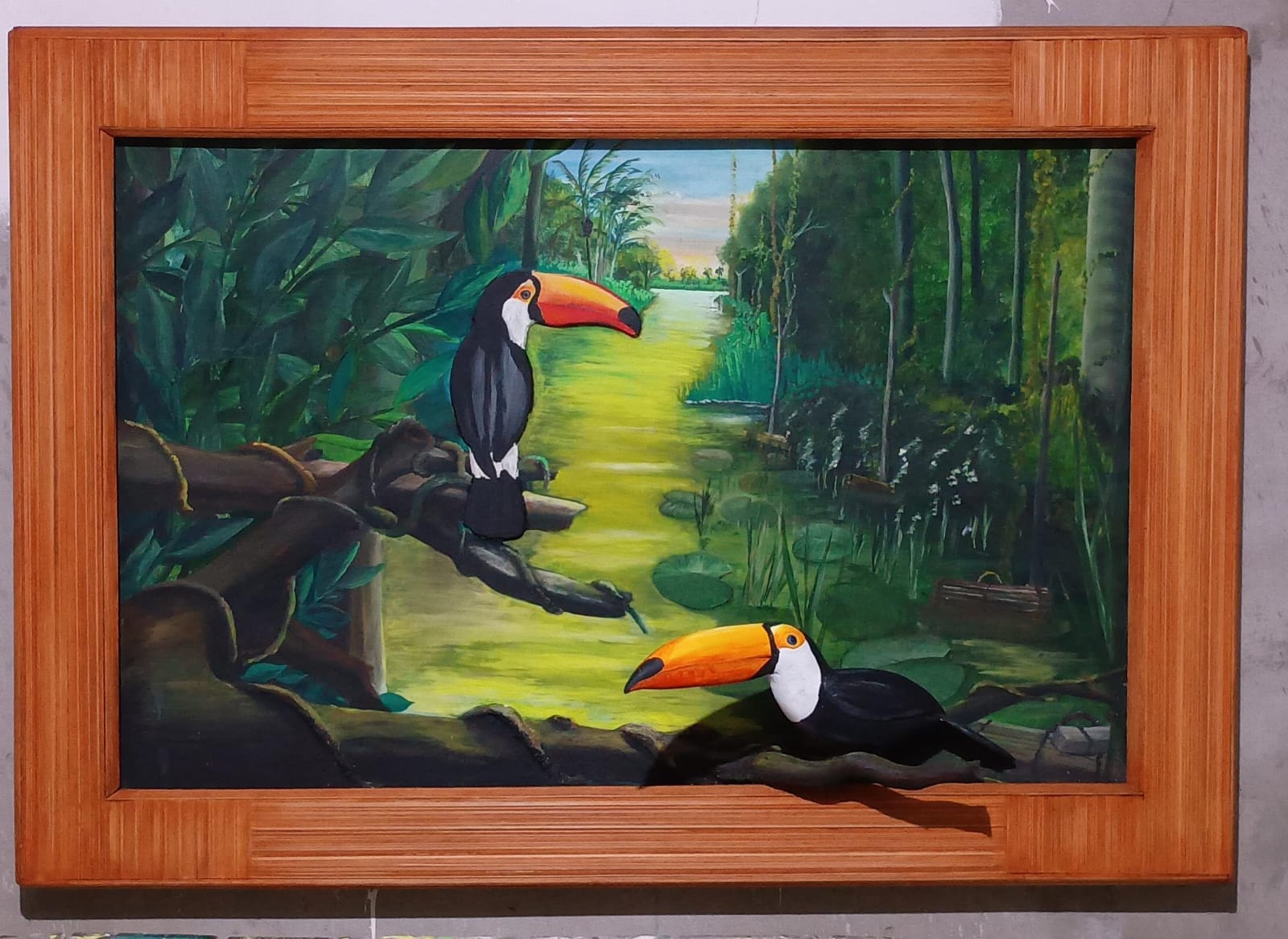 Dois tucanos com bicos grandes e alaranjados são o foco central. Um está pousado de perfil em um galho alto, e o outro está mais abaixo, próximo à base. O fundo mostra um rio que se perde no horizonte entre paredes de floresta verde sob a luz suave do entardecer.